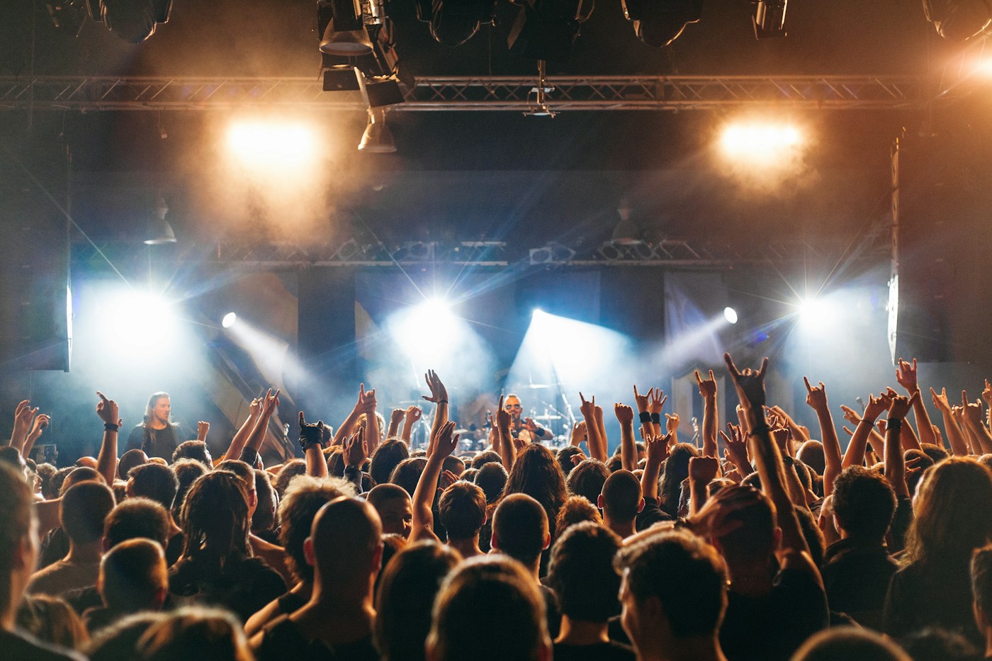 A real concert audience cheering toward a live band beneath stage lighting